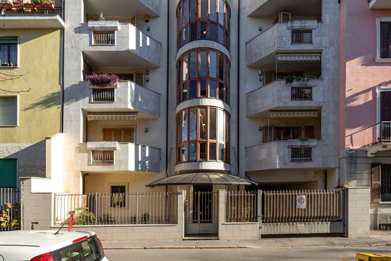 Un edificio a più piani con balconi, una sezione cilindrica centrale e un ingresso chiuso da cancello.