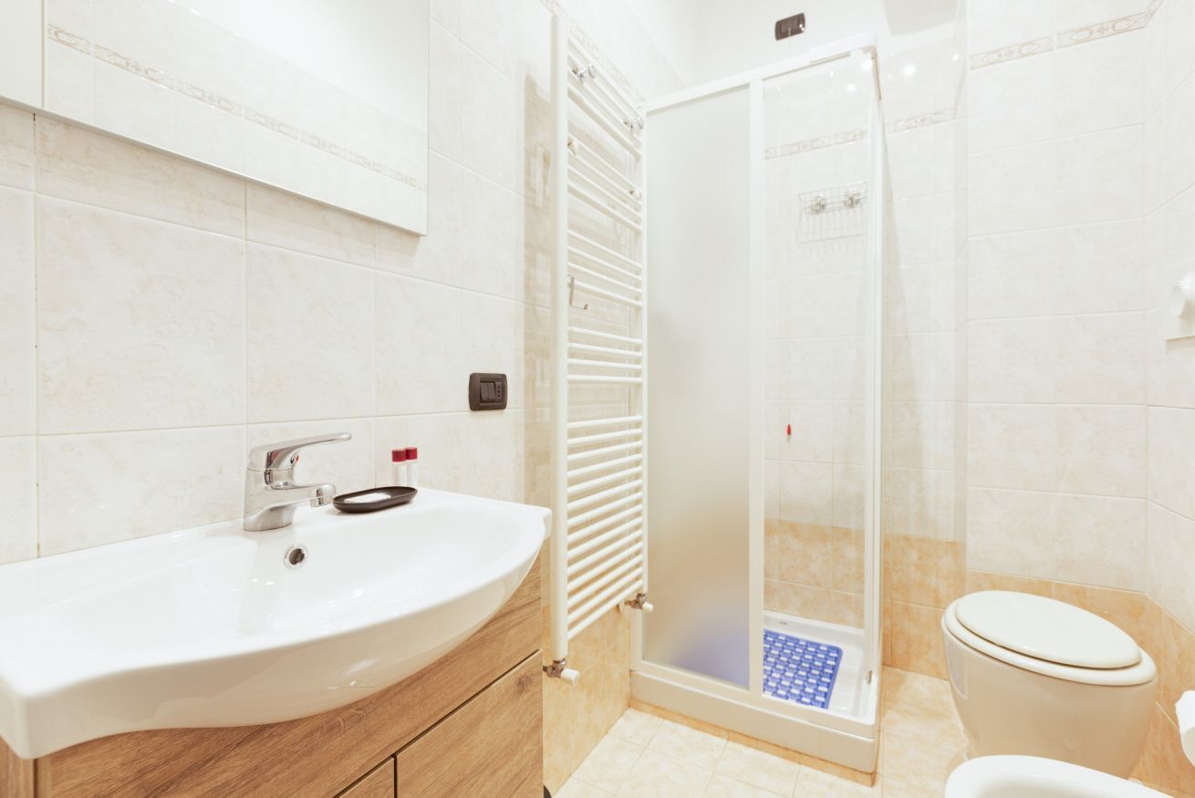 Un bagno con un lavandino bianco, cabina doccia in vetro e un water.