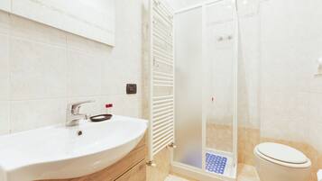 Un bagno con un lavandino bianco, cabina doccia in vetro e un water.