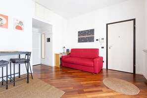 A room with a red sofa, a small table with chairs, a lamp, and a door.