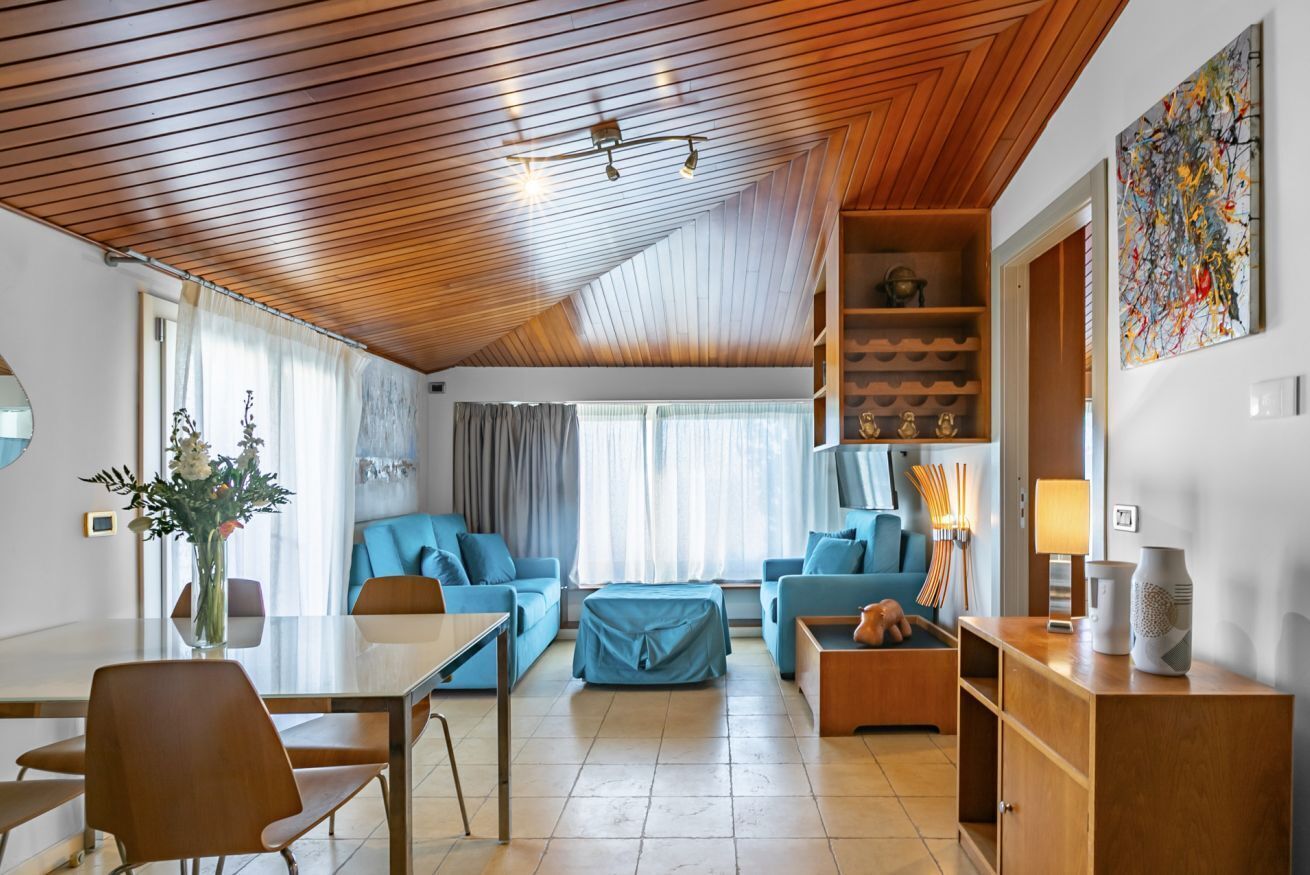Un salon moderne avec un plafond en bois, un coin repas doté d’une table en verre et un ensemble de canapés.