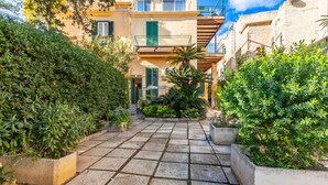 Un patio con suelo de baldosas, rodeado de follaje y edificios con balcones.