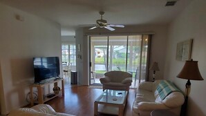 A living room with a television, sofas, a coffee table, a ceiling fan, and a view through a glass door to the outside. - Parker Lakes Heated Pool, Spa and Sports Park <8 miles to Beach, Margaritaville. (Fort Myers)