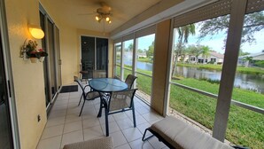 A covered patio with a table and chairs, a ceiling fan, and a view of a lake and greenery. - Parker Lakes Heated Pool, Spa and Sports Park <8 miles to Beach, Margaritaville. (Fort Myers)