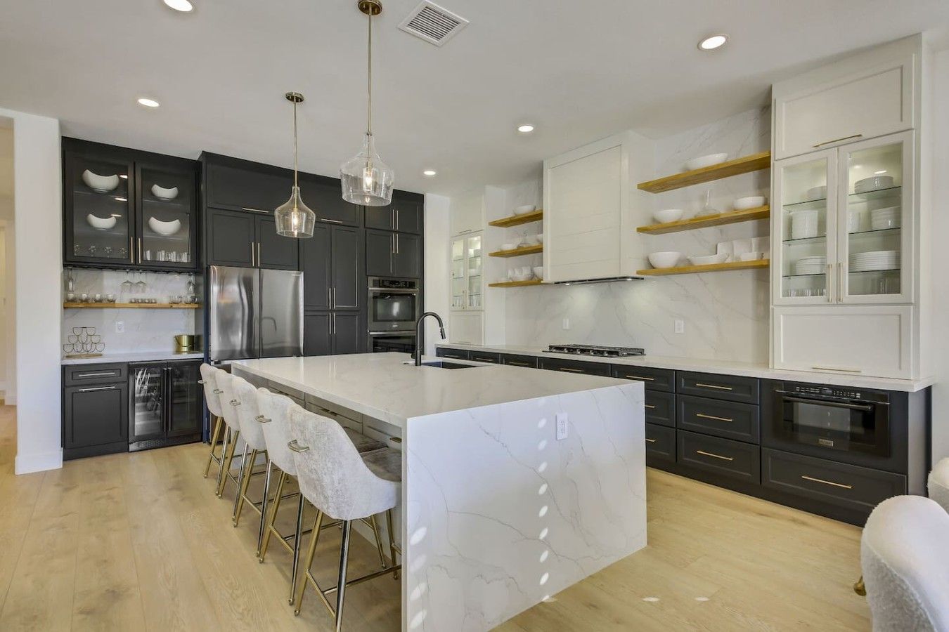 A modern kitchen with a marble island, stainless steel appliances, and a bar seating area.