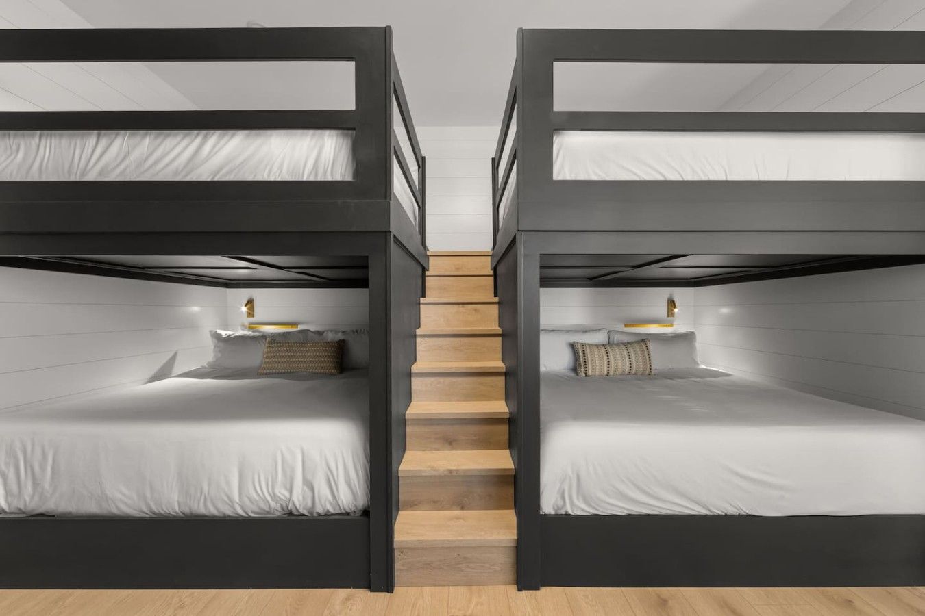 A room with two bunk beds, each with a pillow and a small bedside table.