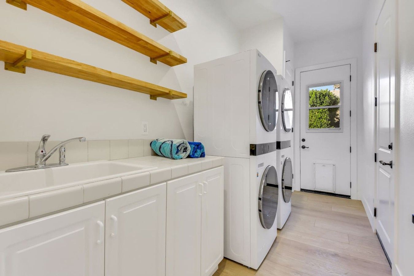 A laundry room with a washing machine, a sink, and wooden shelves.