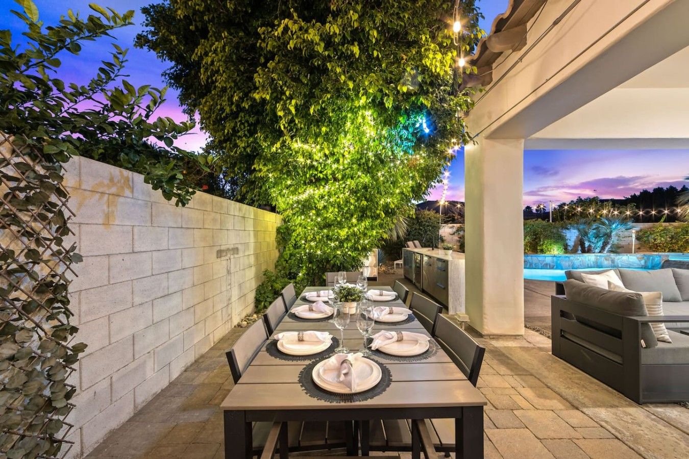 An outdoor dining area with a table set for four, surrounded by a stone wall and a large tree.
