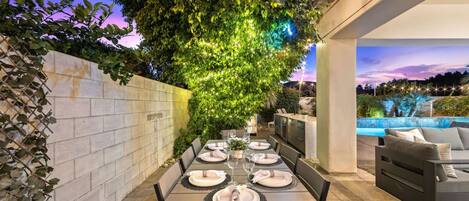 An outdoor dining area with a table set for four, surrounded by a stone wall and a large tree.
