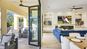 A modern living room with a TV, sofa, and dining area. - Santana: Pool, Spa, BBQ, Fire Pit, Cabanas, Games! (Indio)