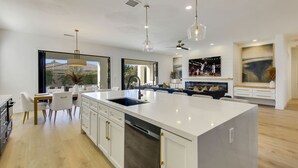 A modern kitchen with a central island, white cabinetry, and pendant lighting. - Santana: Pool, Spa, BBQ, Fire Pit, Cabanas, Games! (Indio)