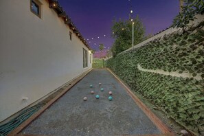 A narrow alleyway with a paved surface, a hedge on one side, and a building on the other.