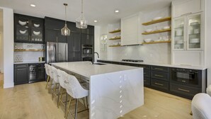 A modern kitchen with a marble island, black and white cabinetry, stainless steel appliances, and pendant lighting. - Santana: Pool, Spa, BBQ, Fire Pit, Cabanas, Games! (Indio)
