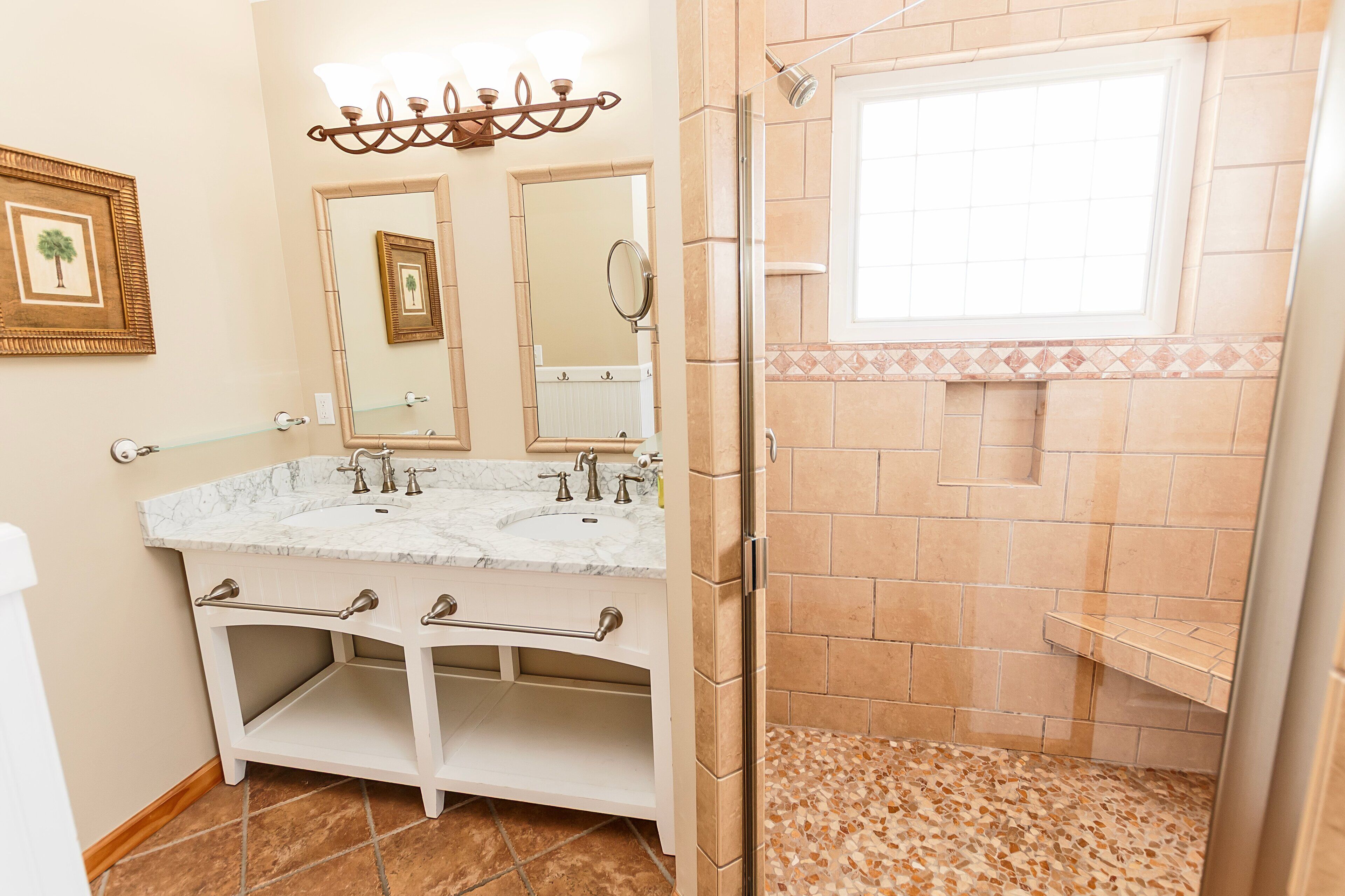 Ein Badezimmer mit Marmorwaschbecken, zwei Spiegeln, einer Dusche mit Fenster und einem gefliesten Boden.