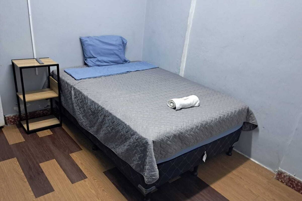 Une petite pièce, bien rangée, avec un lit simple, une table de chevet et un sol à motifs.