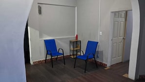 Una habitación con dos sillas azules, una mesita con un objeto rojo y una puerta con el número 2.