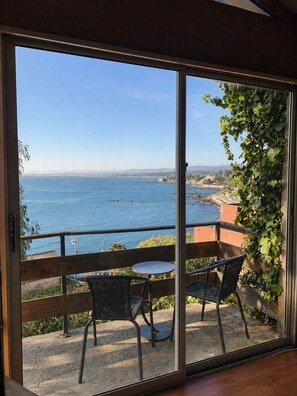 A balcony with a view of the sea, a table, and two chairs.