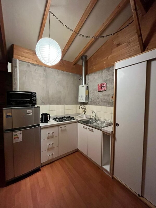 Eine kleine Küche mit Gasherd, Kühlschrank, Spüle und einer Pendelleuchte.