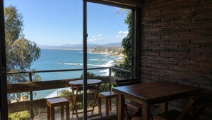 A room with a large window overlooking a beach and ocean, wooden furniture, and a brick wall. - Cabaña con Balcón y Vista al Mar (Concón)