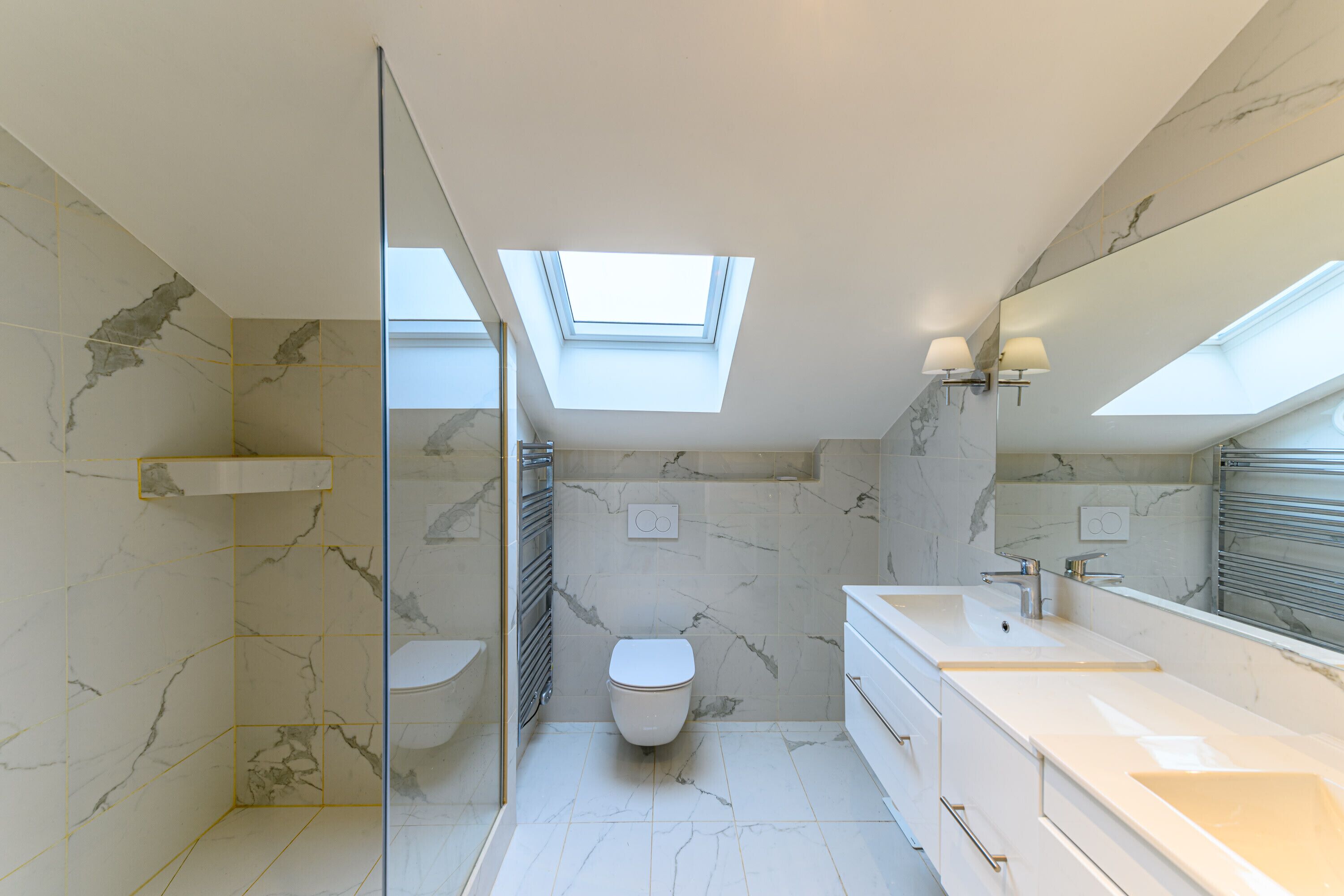 Une salle de bain moderne dotée d’une lucarne, de murs en marbre, d’une douche en verre et d’un grand miroir.