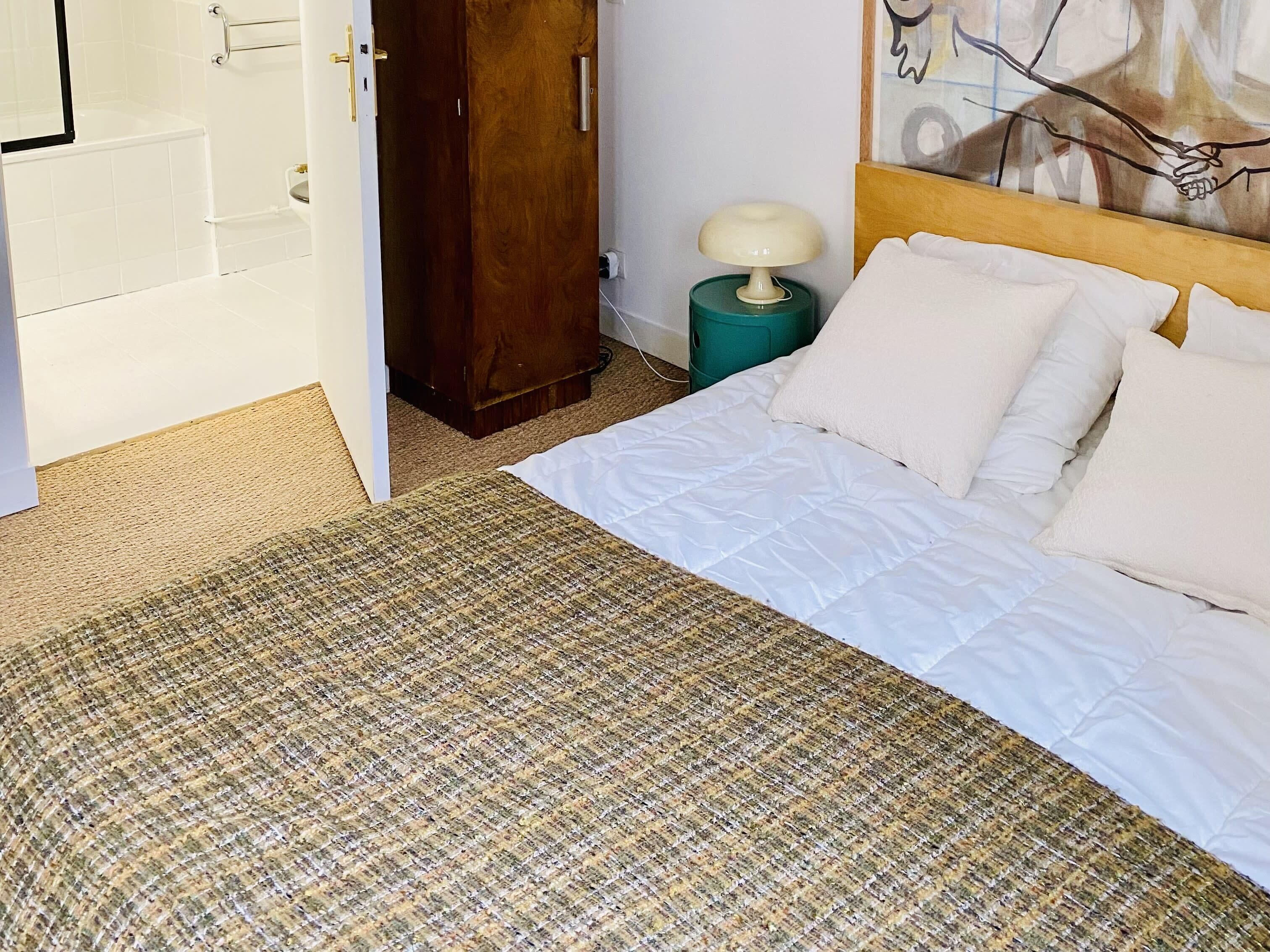 Une chambre à coucher avec un lit, une armoire en bois, une table de chevet verte avec une lampe et un tableau accroché au mur.