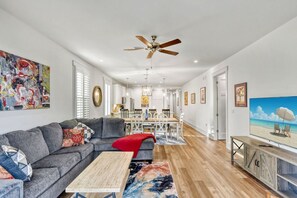 A spacious living room with a grey sectional sofa, a wooden coffee table, and a large painting of a beach scene.