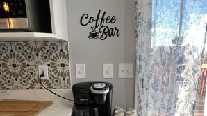 Eine Küche mit Kaffeemaschine, Tassen und einem Wandschild mit der Aufschrift 'Coffee Bar'.