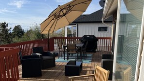 Eine Terrasse mit Gartenmöbeln, darunter Stühle und ein Tisch, sowie ein großer Sonnenschirm.