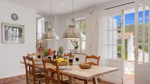 A dining area with a wooden table, chairs, hanging pendant lights, and a view through a glass door to the outside. - 4 bedrooms, sea views, and pure relaxation in Frigiliana. (Frigiliana)