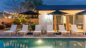 Un espace aménagé au bord de la piscine, avec des chaises longues et des parasols, une terrasse couverte et une piscine.