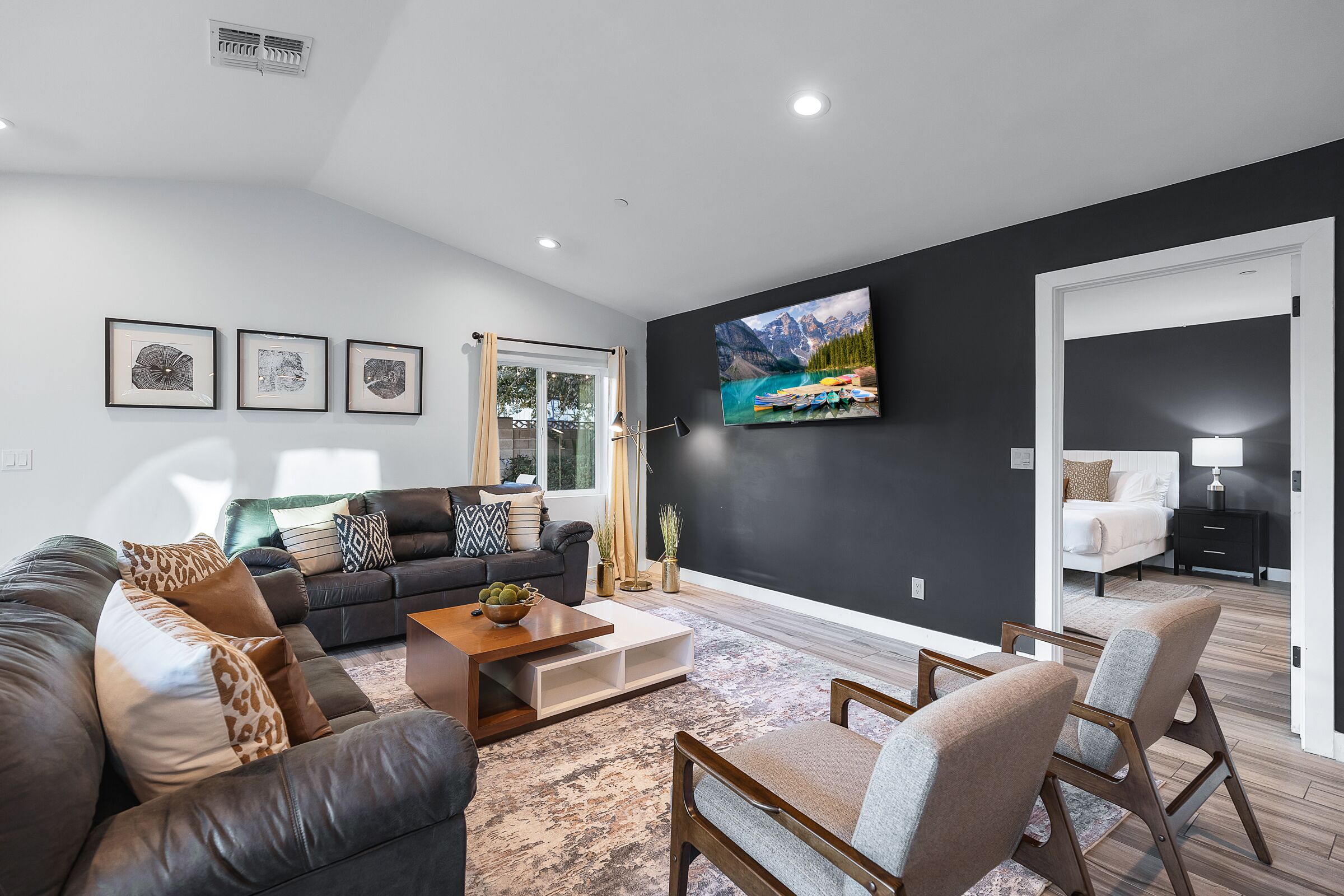 Una sala de estar moderna con una pared de acento negra, un televisor de pantalla plana grande y una zona de estar acogedora con un sofá y sillones de cuero.