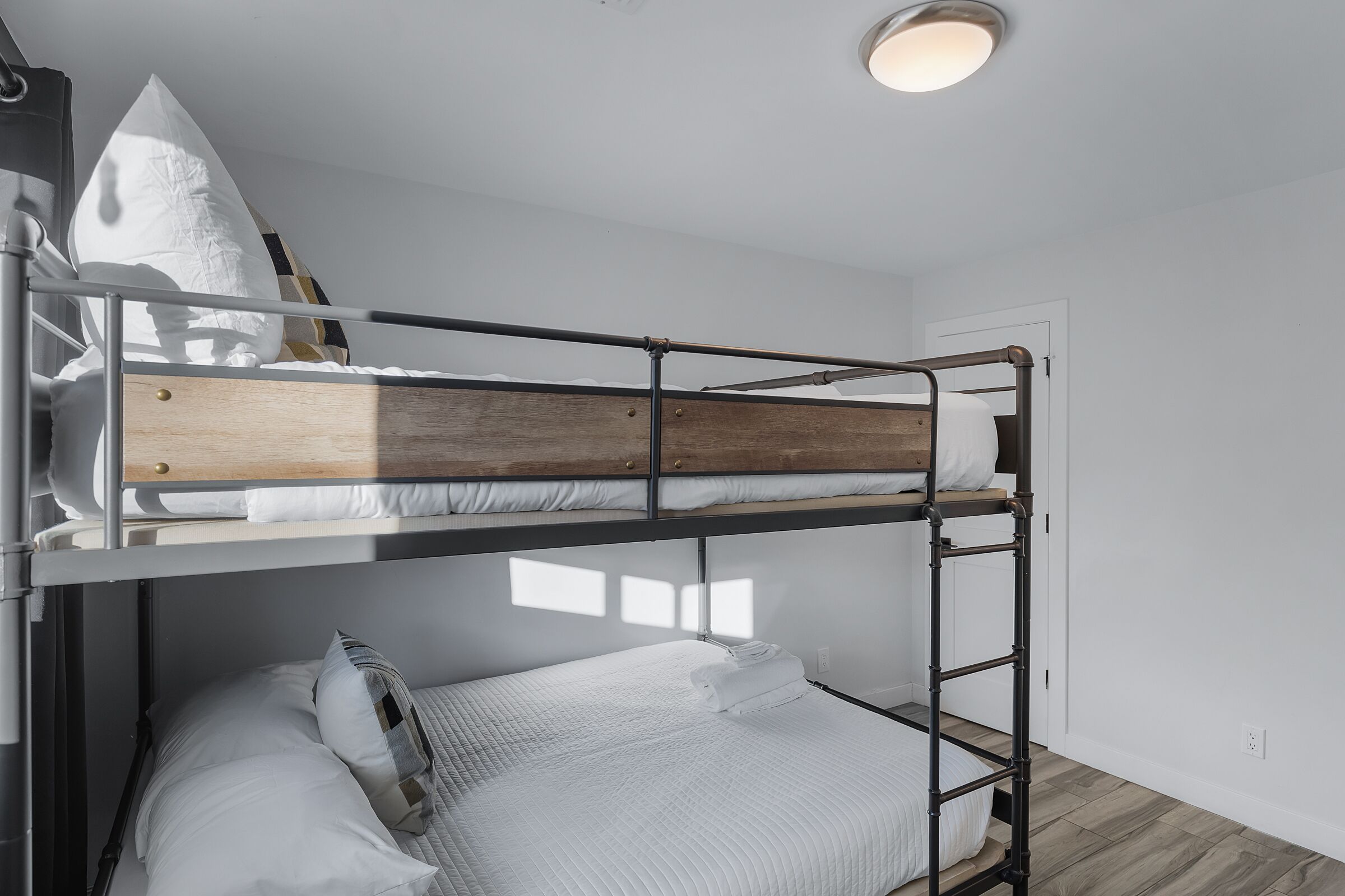Habitación con literas, cabecera de madera, ropa de cama blanca y almohada blanca.