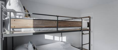 Habitación con literas, cabecera de madera, ropa de cama blanca y almohada blanca.
