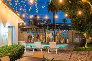 An outdoor pool area with lounge chairs, a cactus mural, and string lights. - Closest Walk to Entertainment District (Scottsdale)