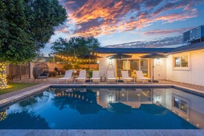 Un jardin avec une piscine, des chaises longues et des guirlandes lumineuses.