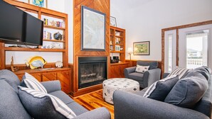 A cozy living room with a fireplace, wooden shelves, and comfortable seating. - Lost Options-Premier Home w/ Tidal Creek Dock; Creek/Marsh Views; Easy Beach Access (Edisto Beach)