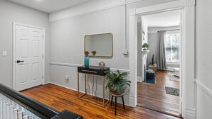 A hallway with a wooden floor, white walls, and a black console table with a mirror and decorative items. - 1 Bed Luxury Downtown Columbia (Elmwood Park) (Columbia)