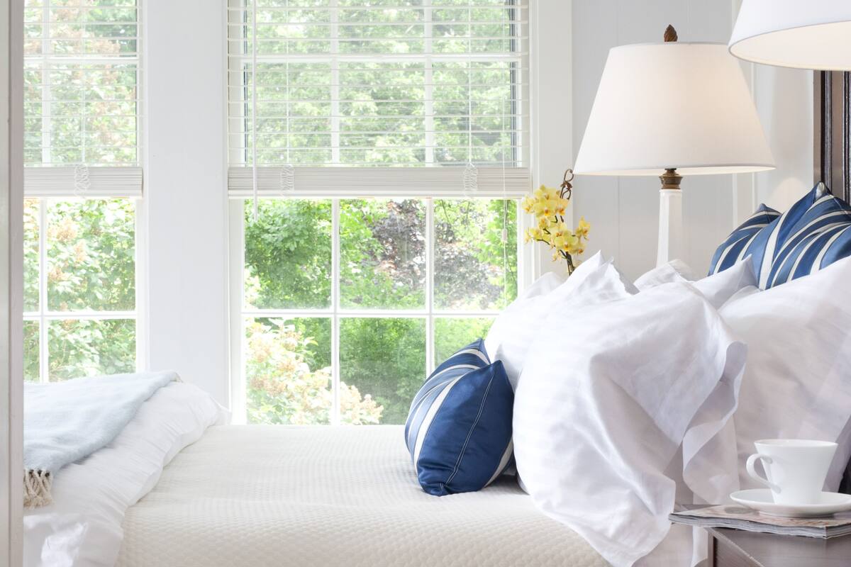 A neatly made bed with white and blue bedding, a white lamp, and a cup on a table beside the bed.
