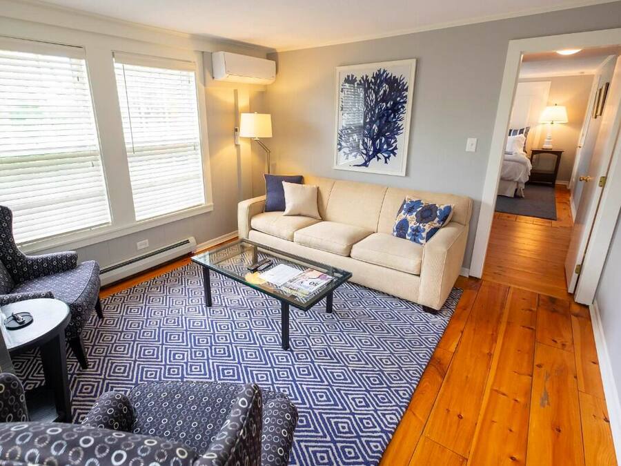 Un salon avec un canapé beige, des fauteuils à motifs, une table basse en verre et un tapis aux motifs bleus et blancs.