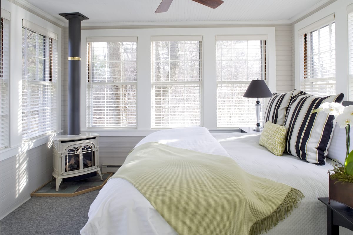 A bedroom with a bed, a window with blinds, a lamp, and a fireplace.