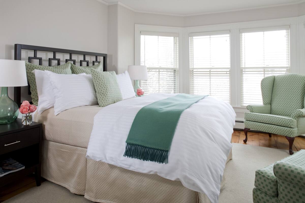 A neatly arranged bedroom with a large bed, two bedside tables, a chair, and a window with blinds.