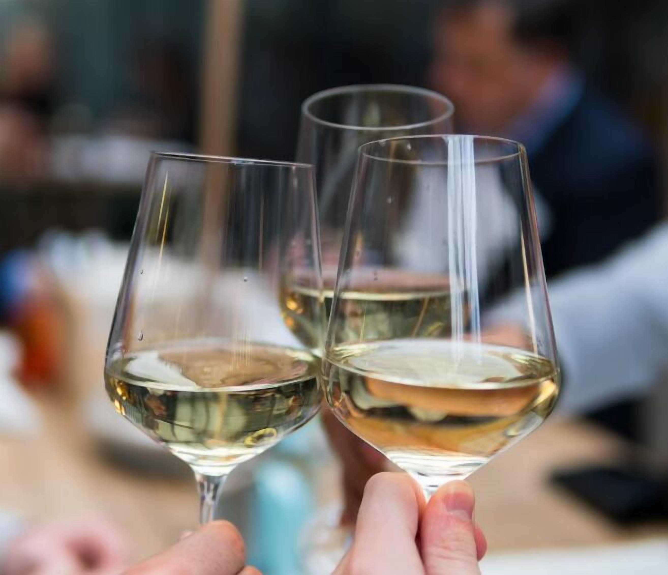 Two wine glasses filled with white wine, held by hands.