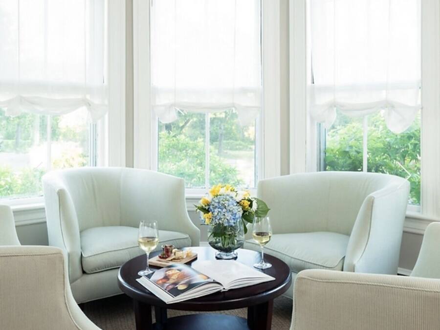 A room with three white armchairs around a round table with a vase of flowers and a magazine.