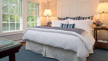 A neatly made bed with white and blue striped pillows, two bedside lamps, and a window with blinds.