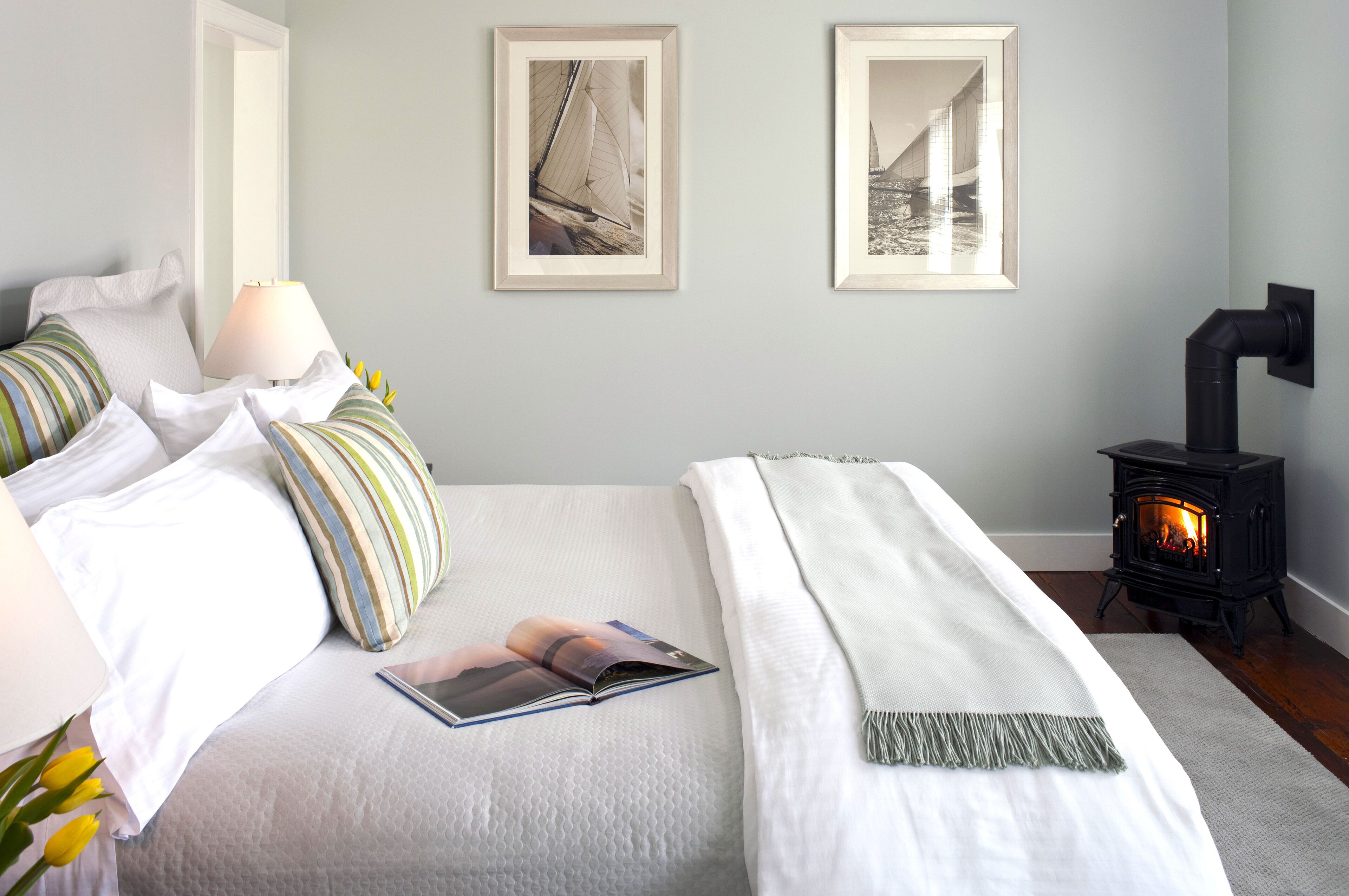 A bedroom with a bed, pillows, a lamp, a framed picture, a fireplace, and a book.