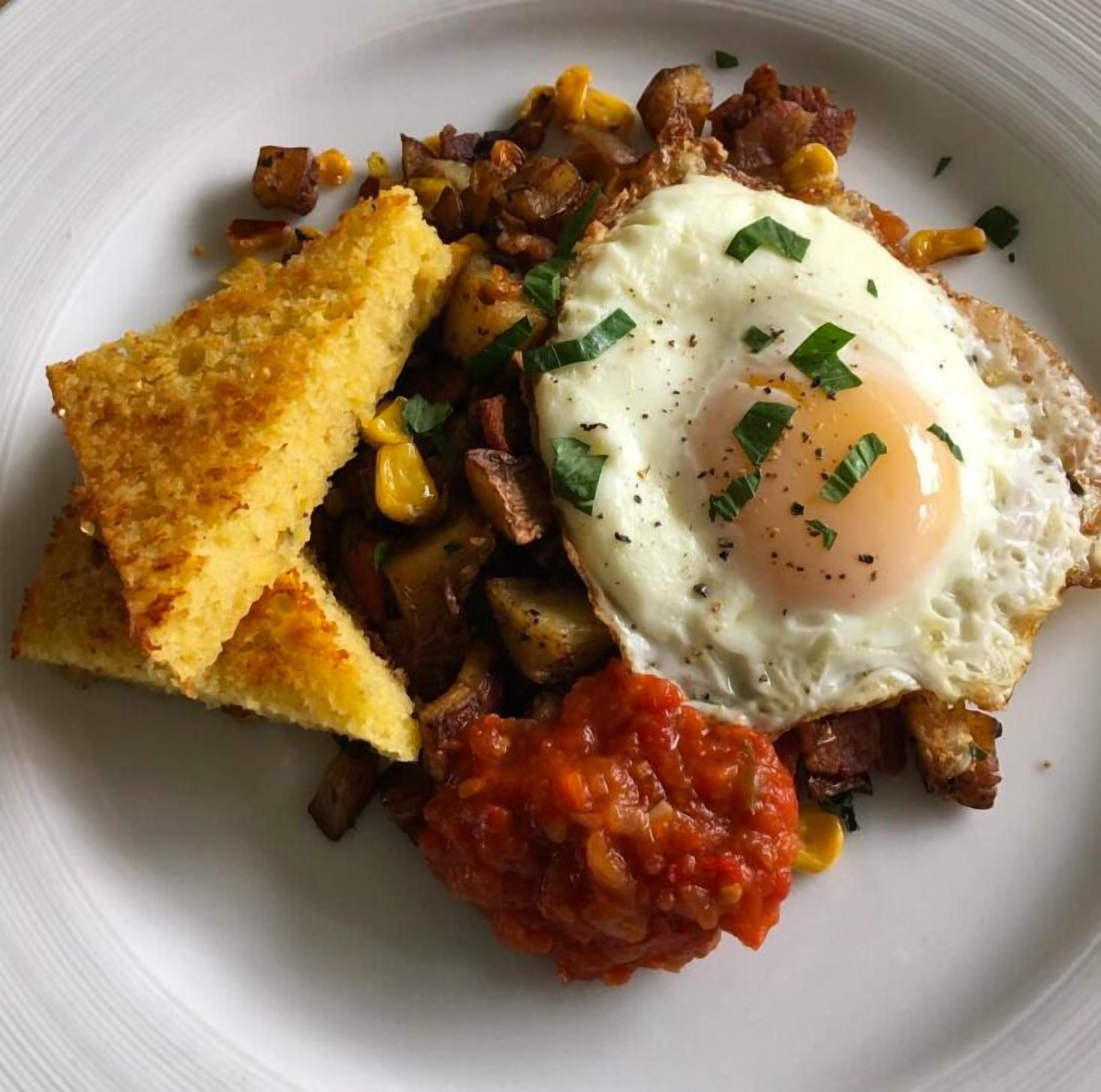 A plate with a fried egg, diced potatoes, corn, and a slice of toast.