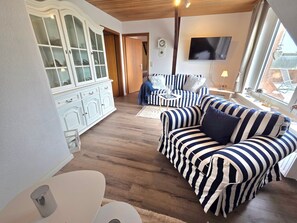 A living room with striped sofas, a cabinet, a television, and a window with a view.