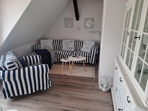 A loft-style room with a sloped ceiling, a striped sofa set, a small round table, and a cabinet with glass doors.