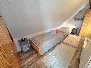 A bedroom with two beds, a nightstand, a lamp, and a wooden wardrobe. - Haus Dorfschmiede, Whg. Ankerplatz - Haus Dorfschmiede (Alkersum)