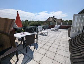 A rooftop terrace with a table and chairs, a red umbrella, and lounge chairs. - Haus Dorfschmiede, Whg. Ankerplatz - Haus Dorfschmiede (Alkersum)